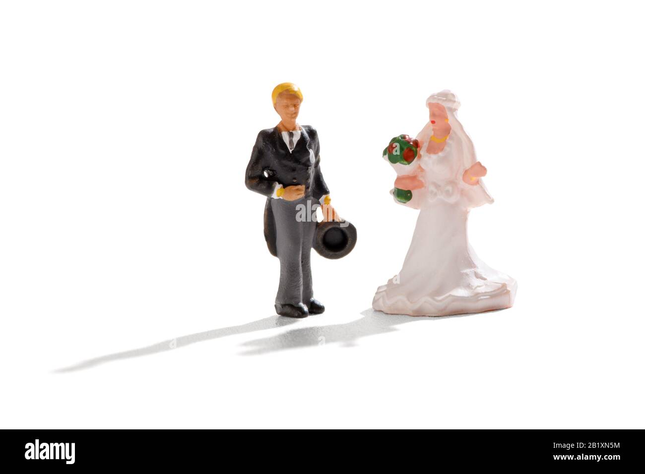 Boda en miniatura con una novia y un novio en la parte superior del sombrero y las colas y una bata blanca de pie juntos en blanco Foto de stock