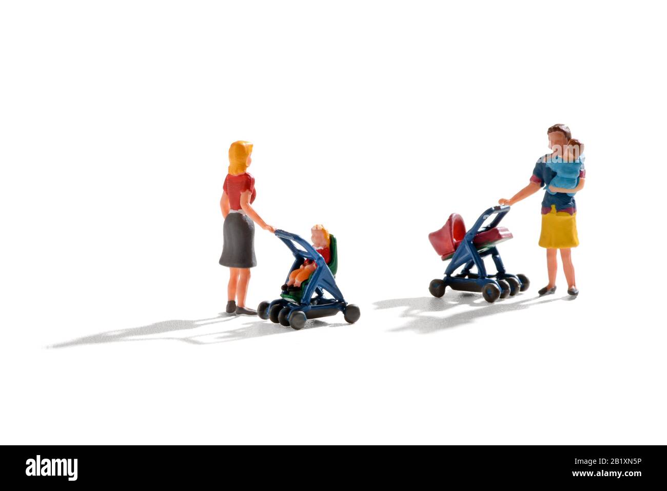 Dos figuras en miniatura de madres jóvenes empujando a sus bebés en un cochecito y cochecito con una sosteniendo a su bebé en sus brazos mientras están charlando en w Foto de stock