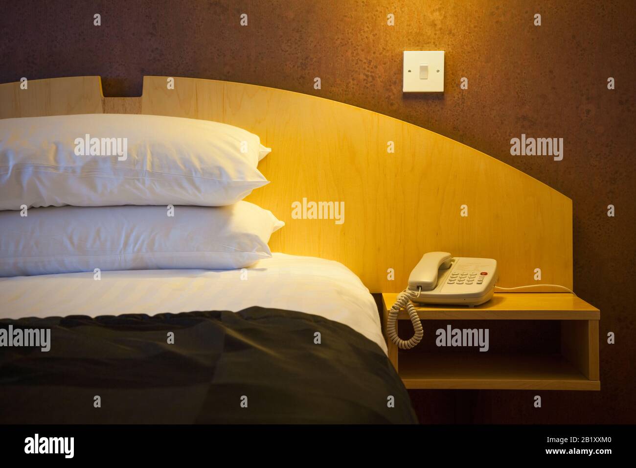 Cama de hotel iluminada con teléfono al lado de la cama por la noche Foto de stock