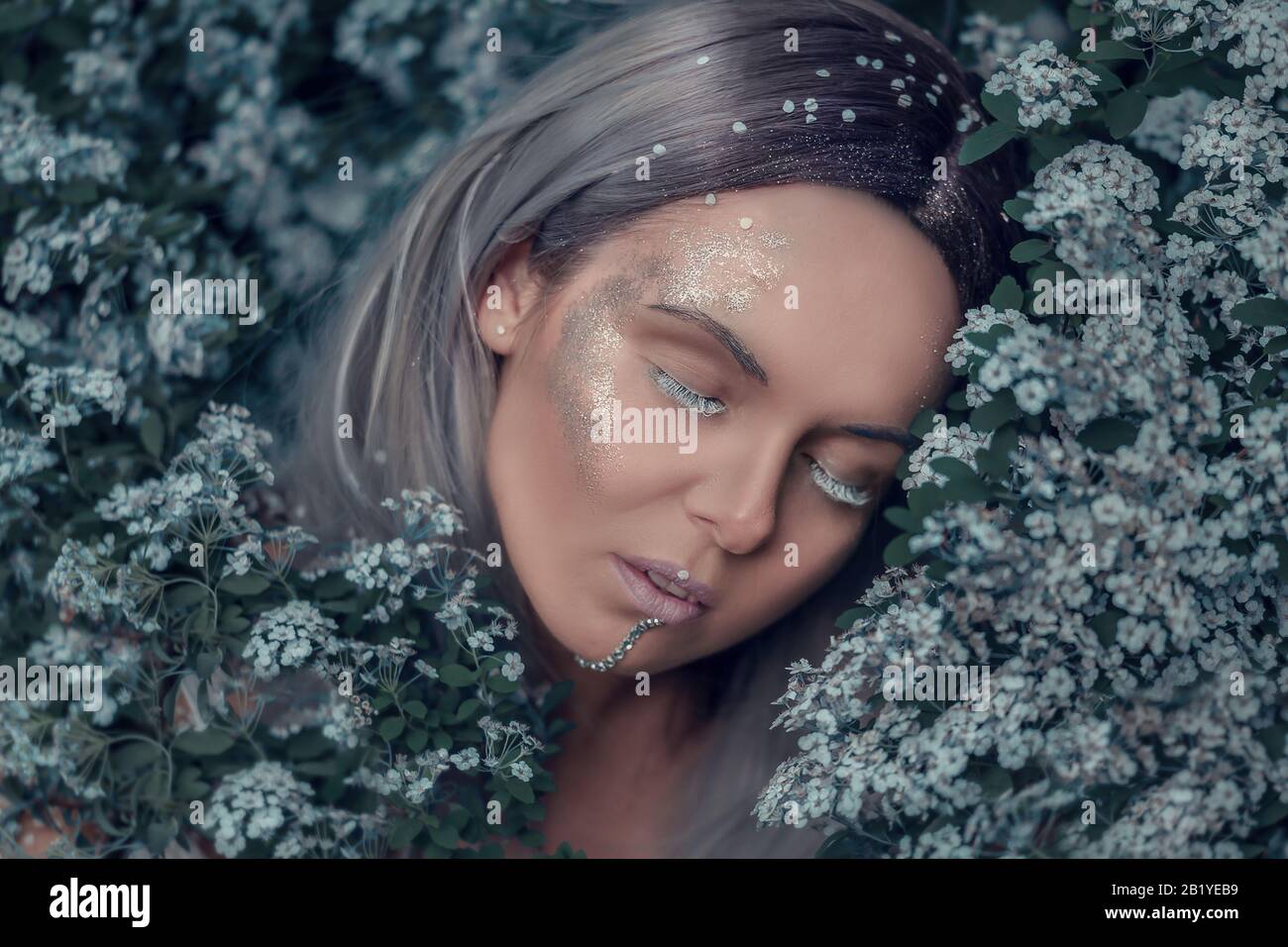 Cuento de hadas bosque ninfa, hermosa mujer sexy con el pelo blanco y gris en el jardín de primavera, dormir en el árbol en flor, estilo de moda de ensueño vintage Foto de stock