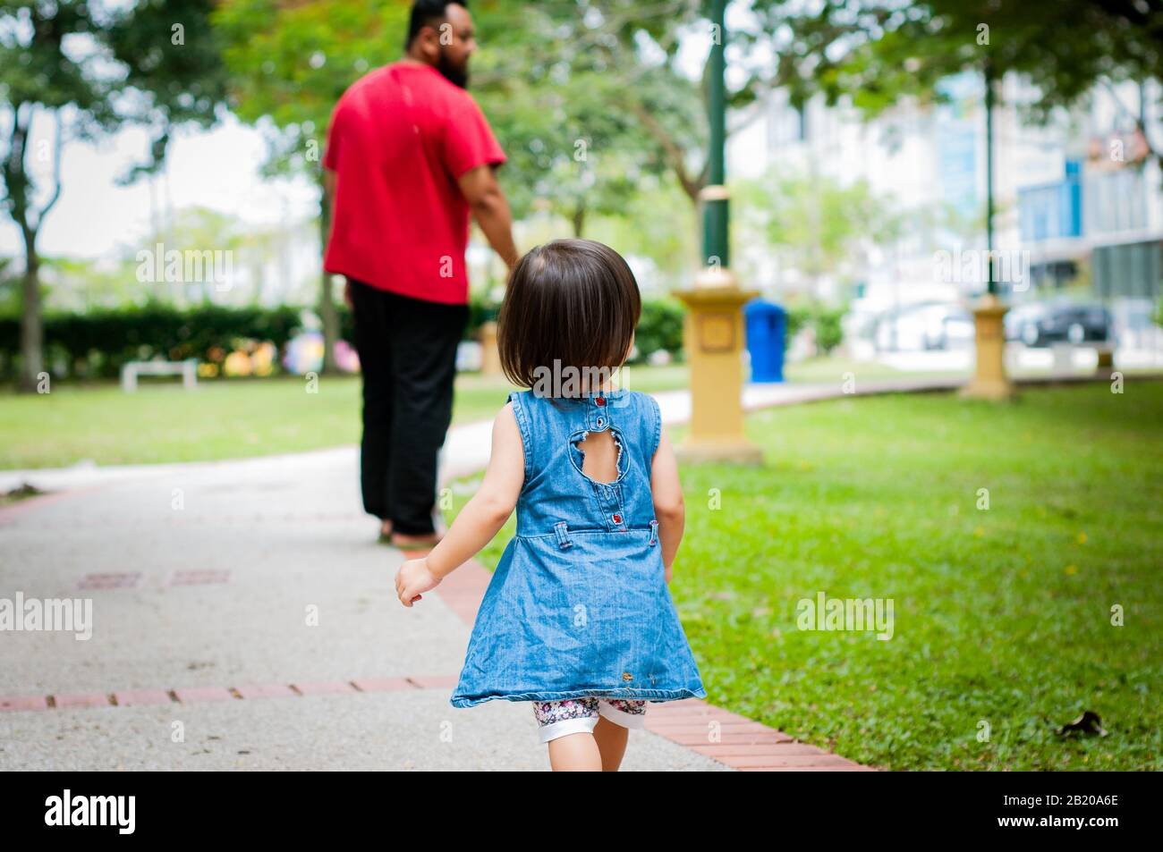 1 asiático-año-viejo niño está ocupado caminando con su padre en un parque tropical en la mañana. La exploración y el concepto de paternidad. Foto de stock