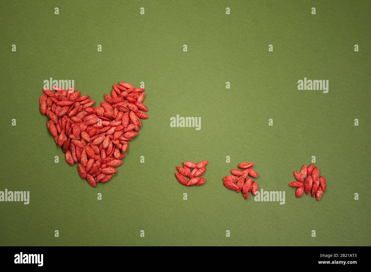corazón rojo y tres puntos de semillas de pepino sobre fondo verde con lugar para texto, minimalismo Foto de stock