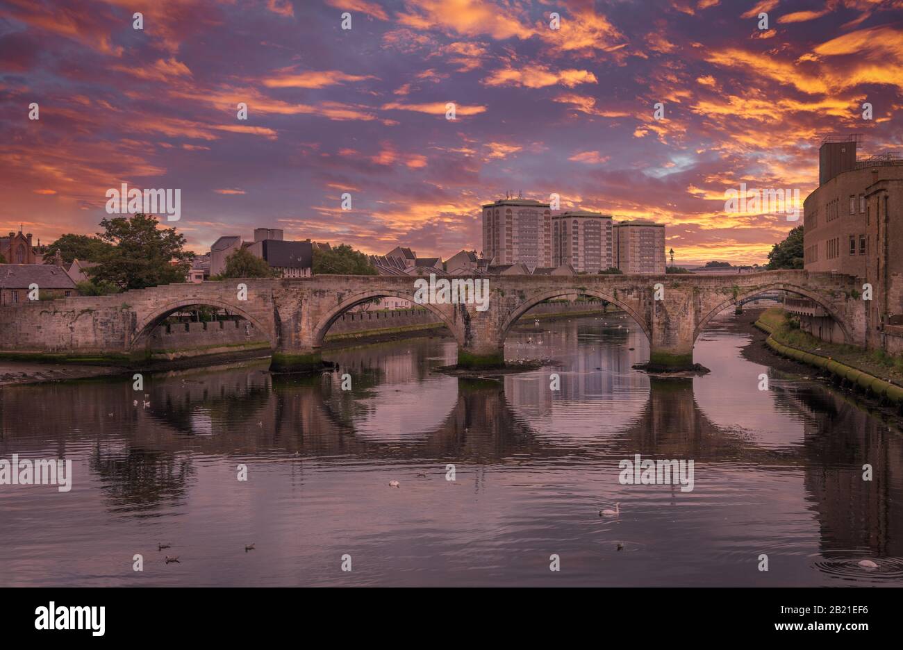 El histórico Puente Viejo de Ayr en Escocia que se extiende por el río Ayr y una espectacular puesta de sol roja sobre la ciudad. Foto de stock
