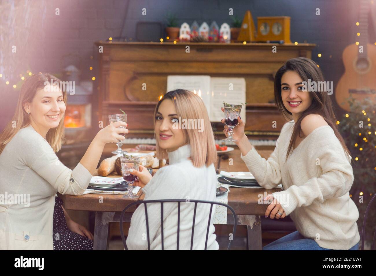Contento mujeres jóvenes en ropa informal con copas de cócteles con bayas rojas en la mesa festiva durante las vacaciones de Navidad Foto de stock
