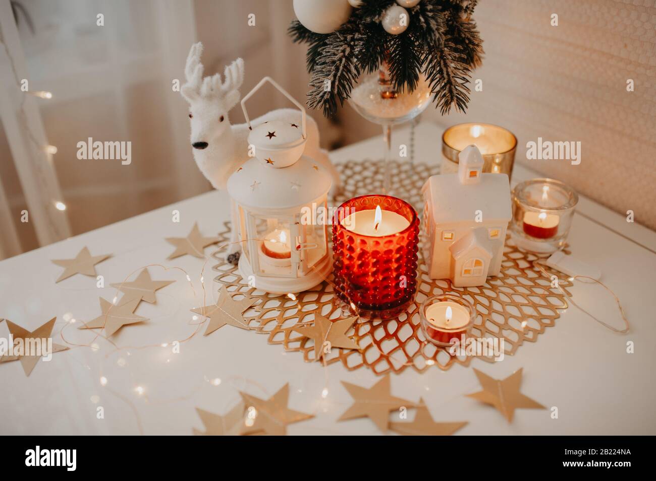 Decoración de mesa blanca para Navidad y año Nuevo, quema de velas blancas  y rojas, un candelabro de forma de linterna en servilleta marrón mimbre,  figura de un Fotografía de stock -