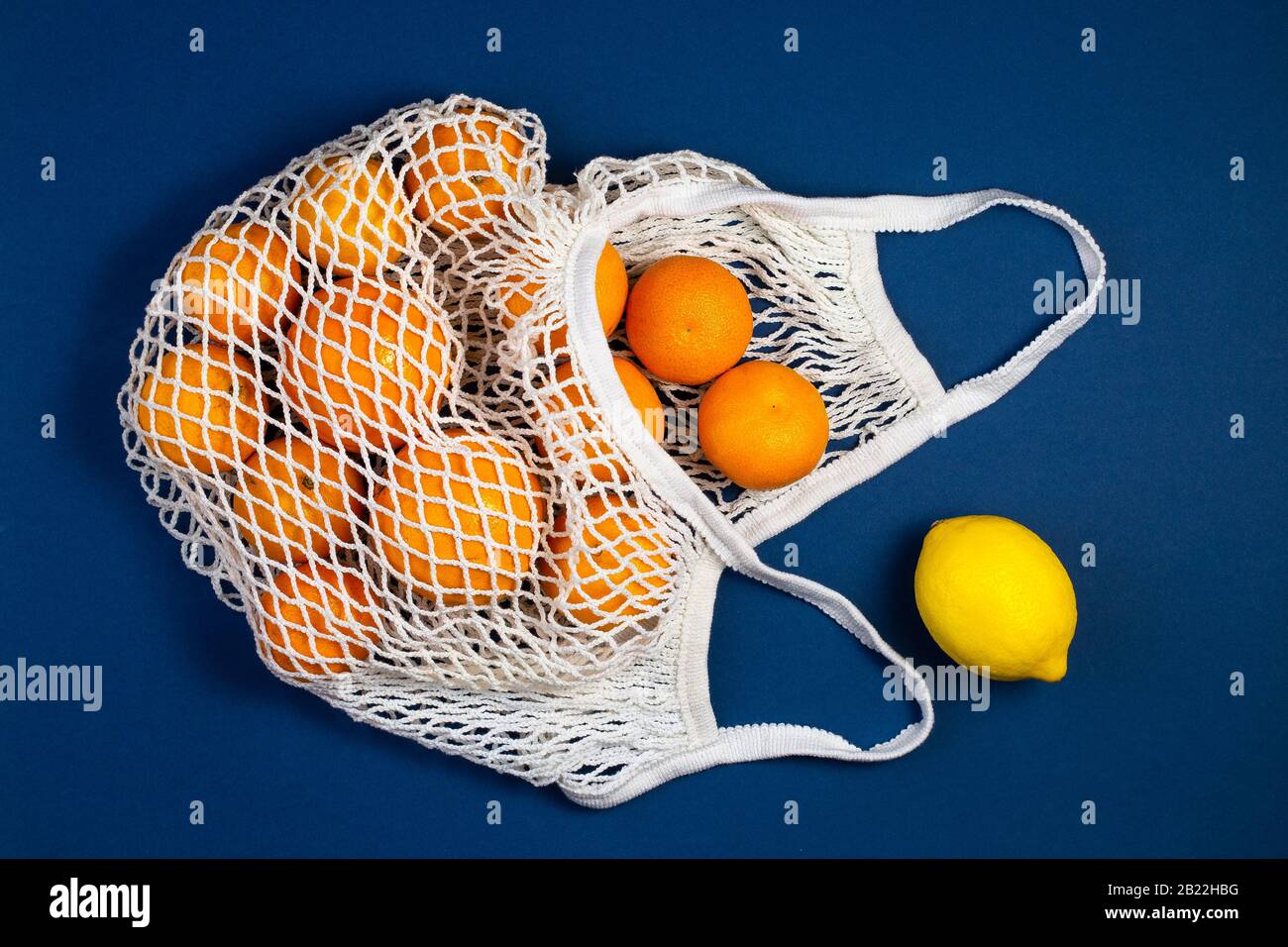 Bolsa de compras de malla con tangerinas, limones sobre un fondo clásico azul. Plano, vista superior. Sin residuos, concepto sin plástico. Comer limpio y saludable muere Foto de stock