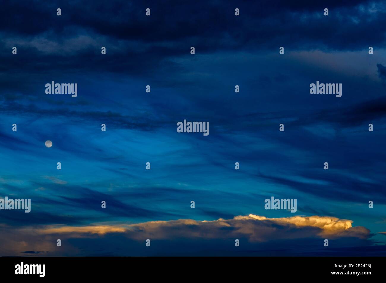 Espectacular paisaje nocturno azul a capas con luna y pequeñas nubes blancas Foto de stock