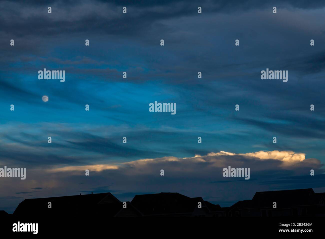 Paisaje nocturno, con cielo azul en capas, luna, rayas de nubes brillantes y siluetas Foto de stock