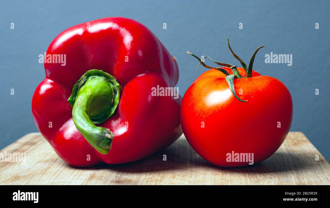 tomate y pimiento rojo dulce de pimentón sobre un plato de madera sobre fondo gris. verduras frescas y saludables. Foto de stock