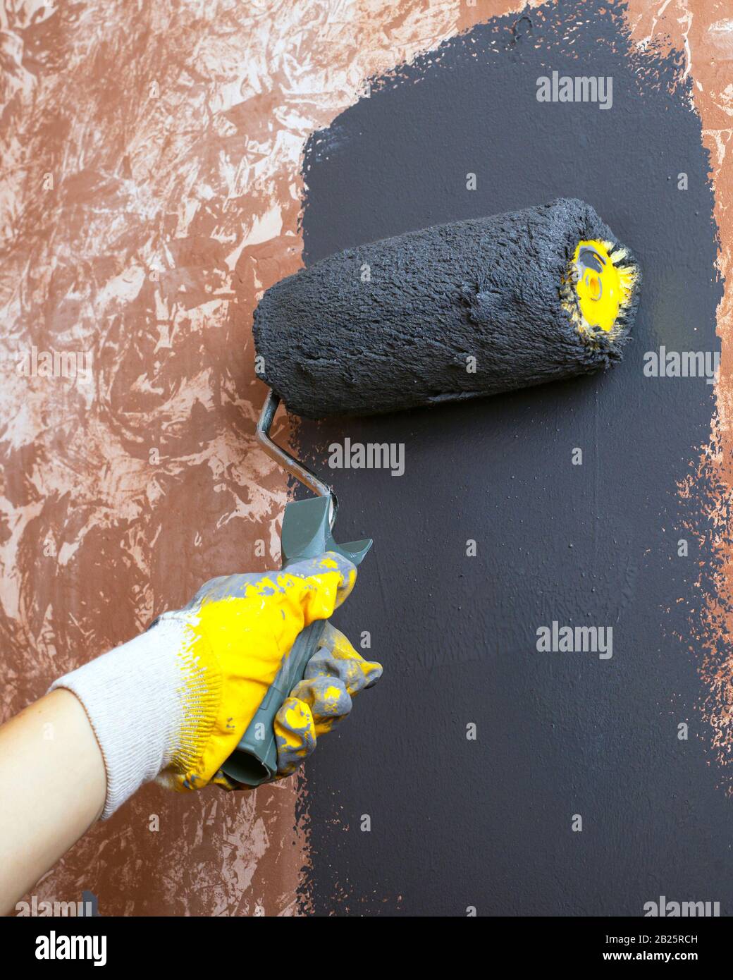 pared de casa pintada a mano con pintura acrílica gris con un rodillo en  guantes de trabajo amarillos Fotografía de stock - Alamy