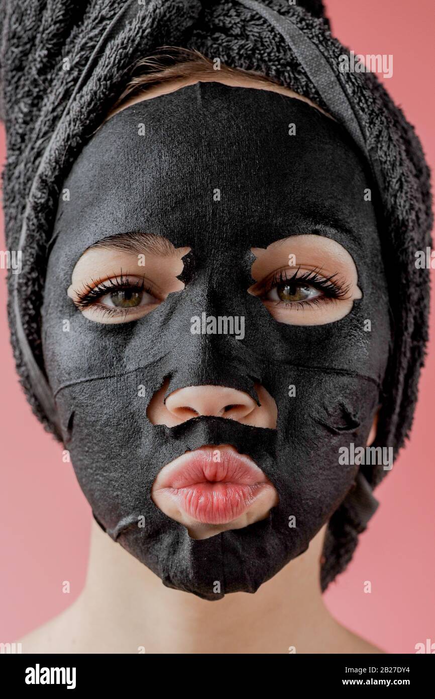 Mujer joven aplique máscara facial de tela cosmética negra sobre fondo  rosa. Mascarilla facial peeling con carbón, tratamiento de belleza spa,  cuidado de la piel, cosmetología Fotografía de stock - Alamy