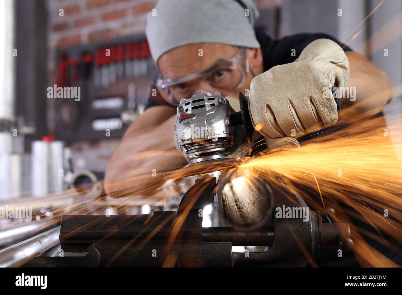 El hombre trabaja en casa el taller garaje con amoladora, gafas y guantes de construcción, lijado metal hace chispas closeup, bricolaje y concepto de artesanía Foto de stock