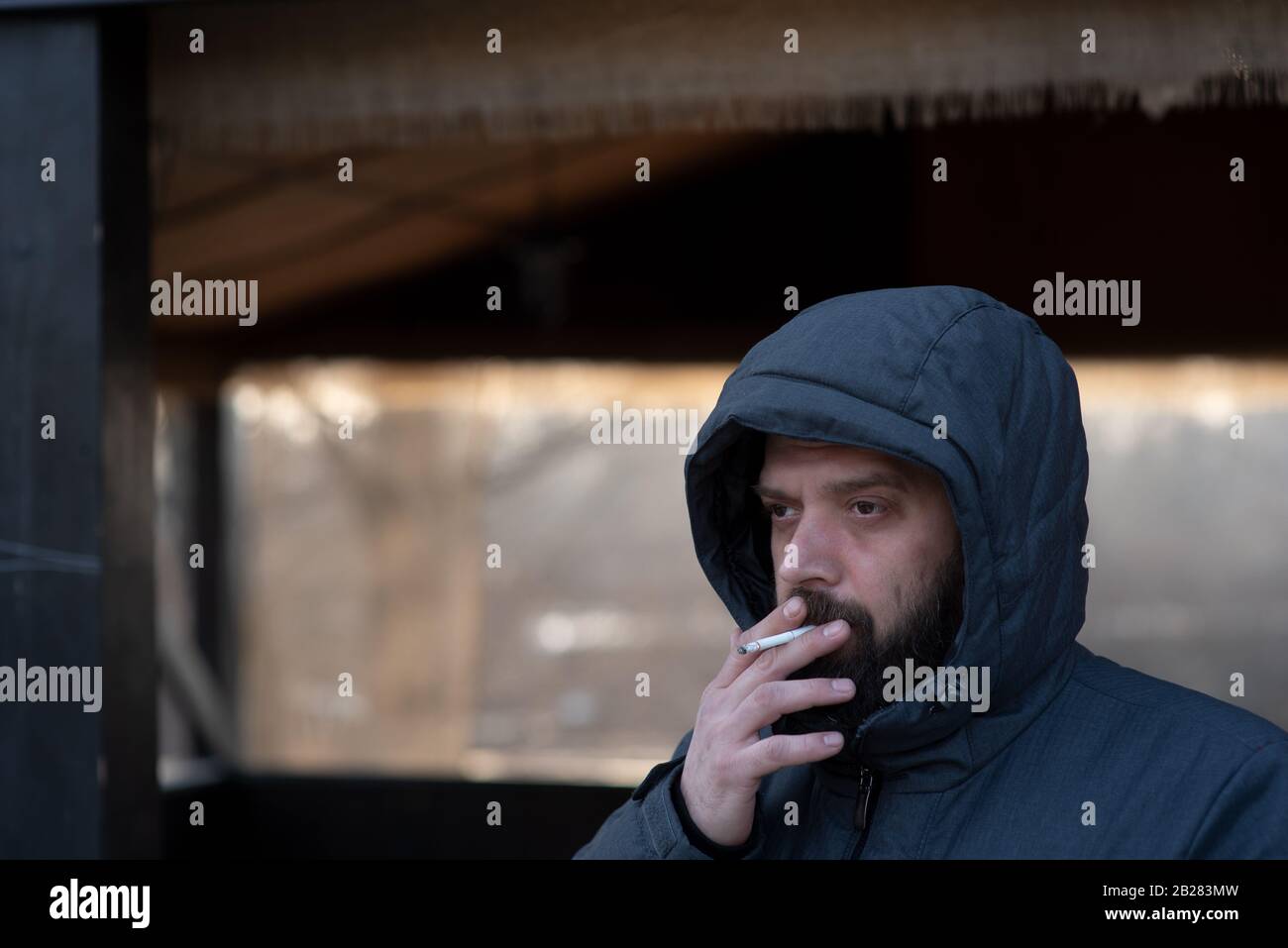 Retrato del hombre en una campana con cigarrillo. Hombre con barba en una chaqueta gris en la calle. Retrato de un hombre. El tipo con la barba. Invierno, invierno Foto de stock