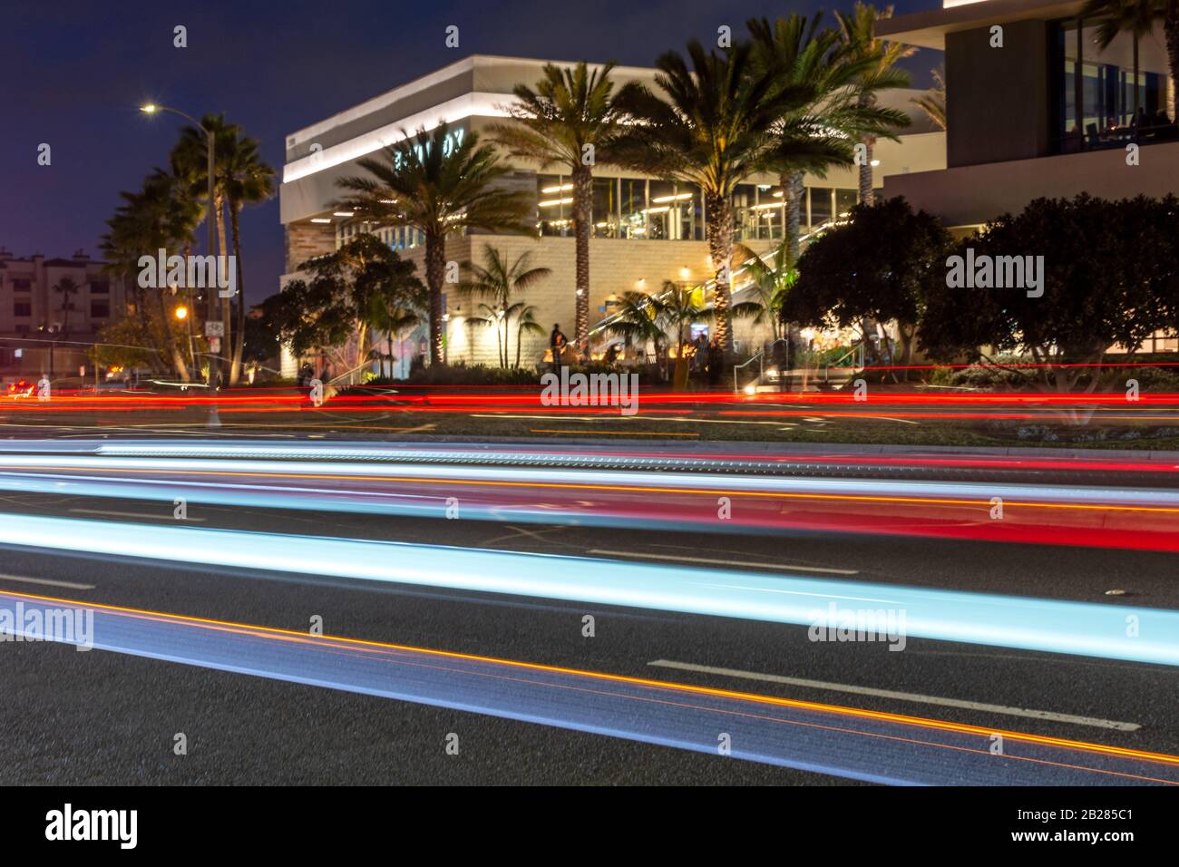 Coloridos senderos de luz en una carretera de la ciudad frente a edificios iluminados por la noche. Foto de stock