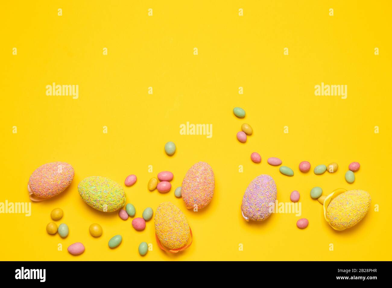 Coloree los huevos de Pascua y los sabrosos granos de gelatina de caramelo de color sobre un fondo amarillo con espacio para copias, vista superior, disposición plana. Foto horizontal Foto de stock