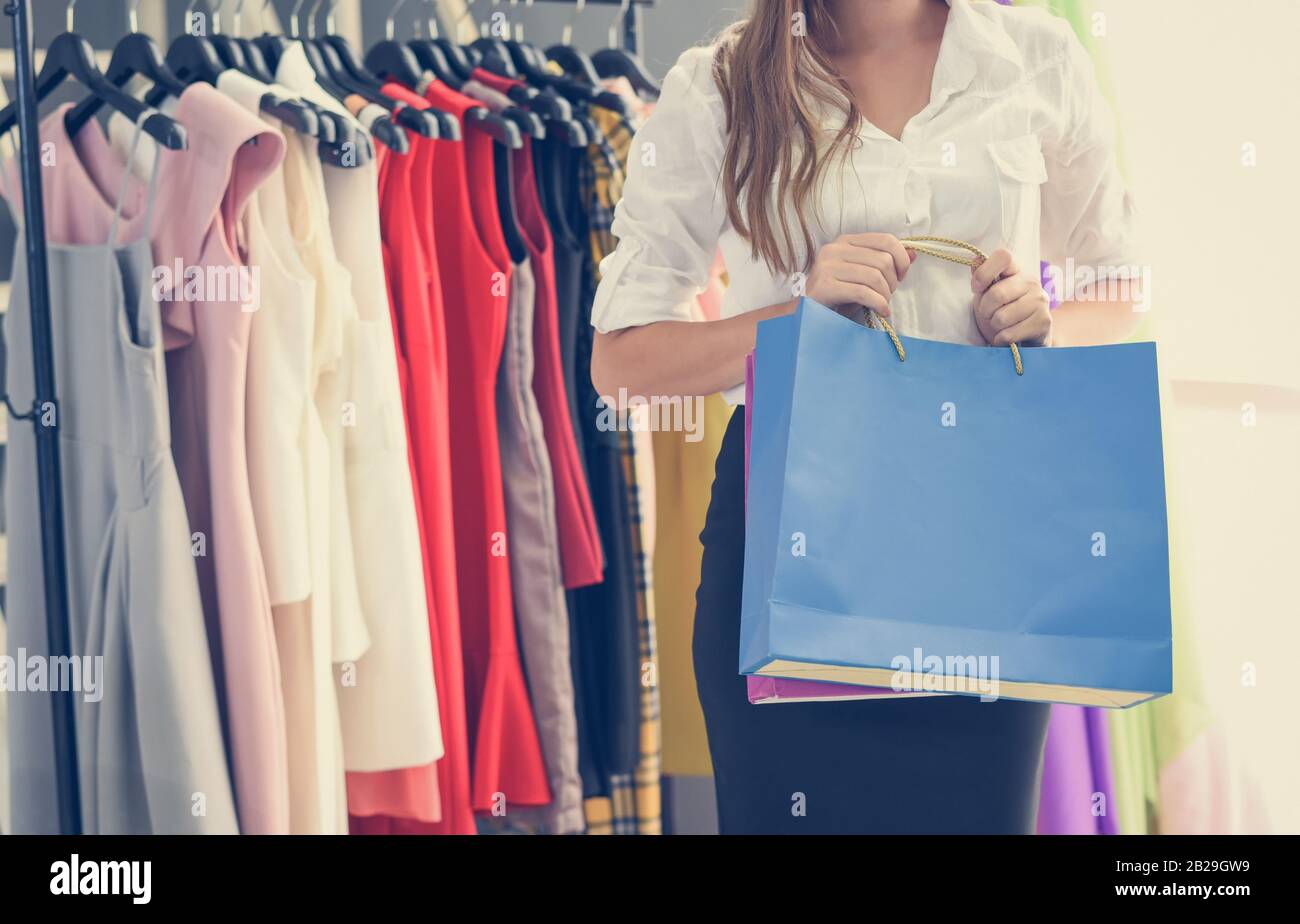 Mujer de compras y la celebración de la bolsa de compras en la tienda de  ropa de moda de las mujeres con vestidos de mujeres de colores en las  perchas en una