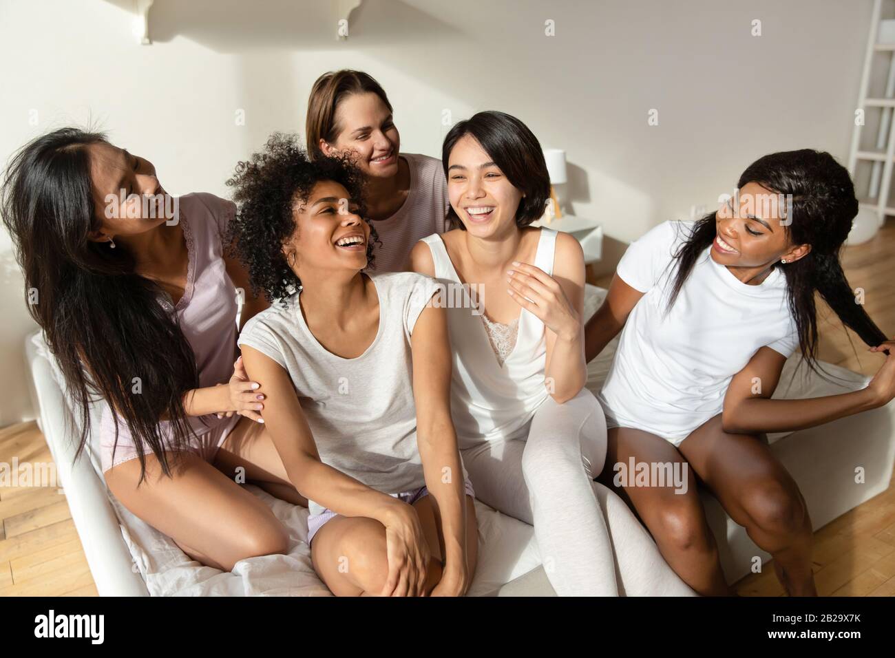 Felices y diversas chicas charlando y riendo, sentados en la cama juntos Foto de stock
