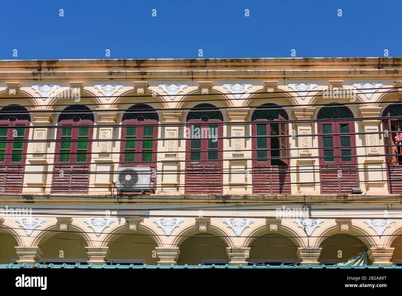 Cables eléctricos estirados frente a un edificio sino-portugués con muchas ventanas, Tailandia Foto de stock