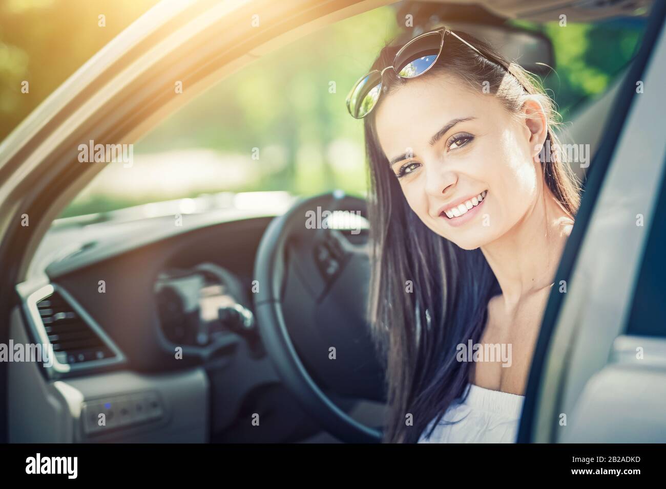 Hermosa mujer joven sentada en el interior de un coche nuevo con una sonrisa. Se alegra de que sea un conductor. Foto de stock