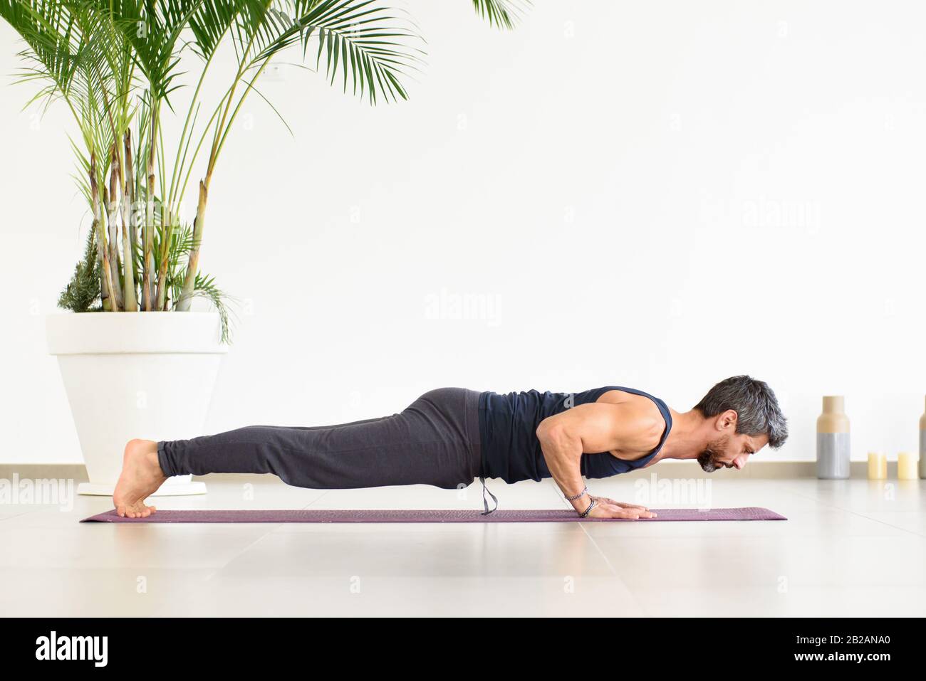 Ajuste al hombre haciendo yoga chaturanga push-ups durante su entrenamiento en un gimnasio de alta llave con la palma en maceta en una vista lateral de ángulo bajo en un concepto de salud y fitness Foto de stock