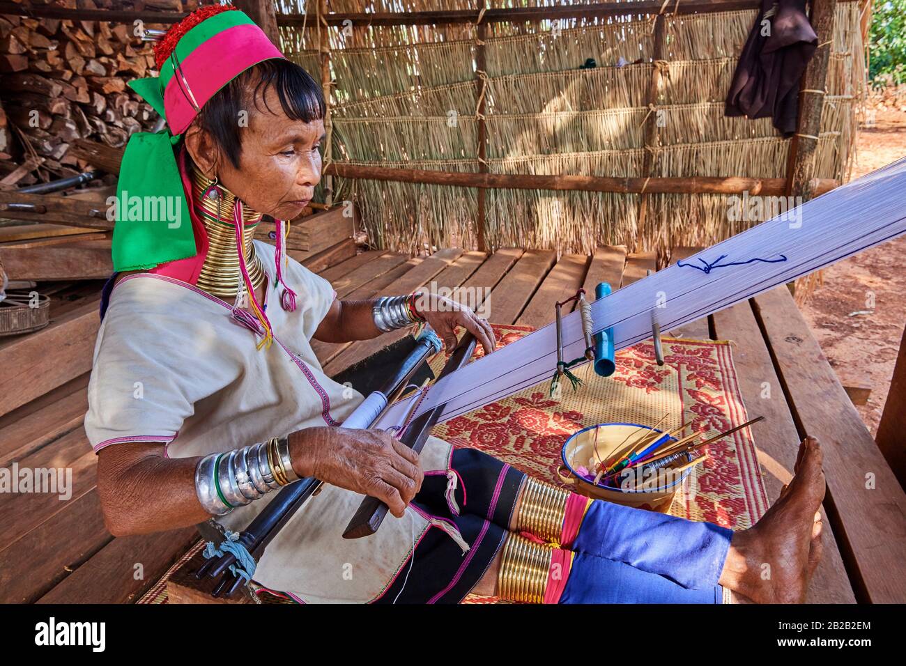 Mujer Kayan Lahwi con bobinas de latón en el cuello y ropa tradicional hilando algodón en su tienda. Ella ha mostrado detrás de ella el tejido de mano que ella Foto de stock