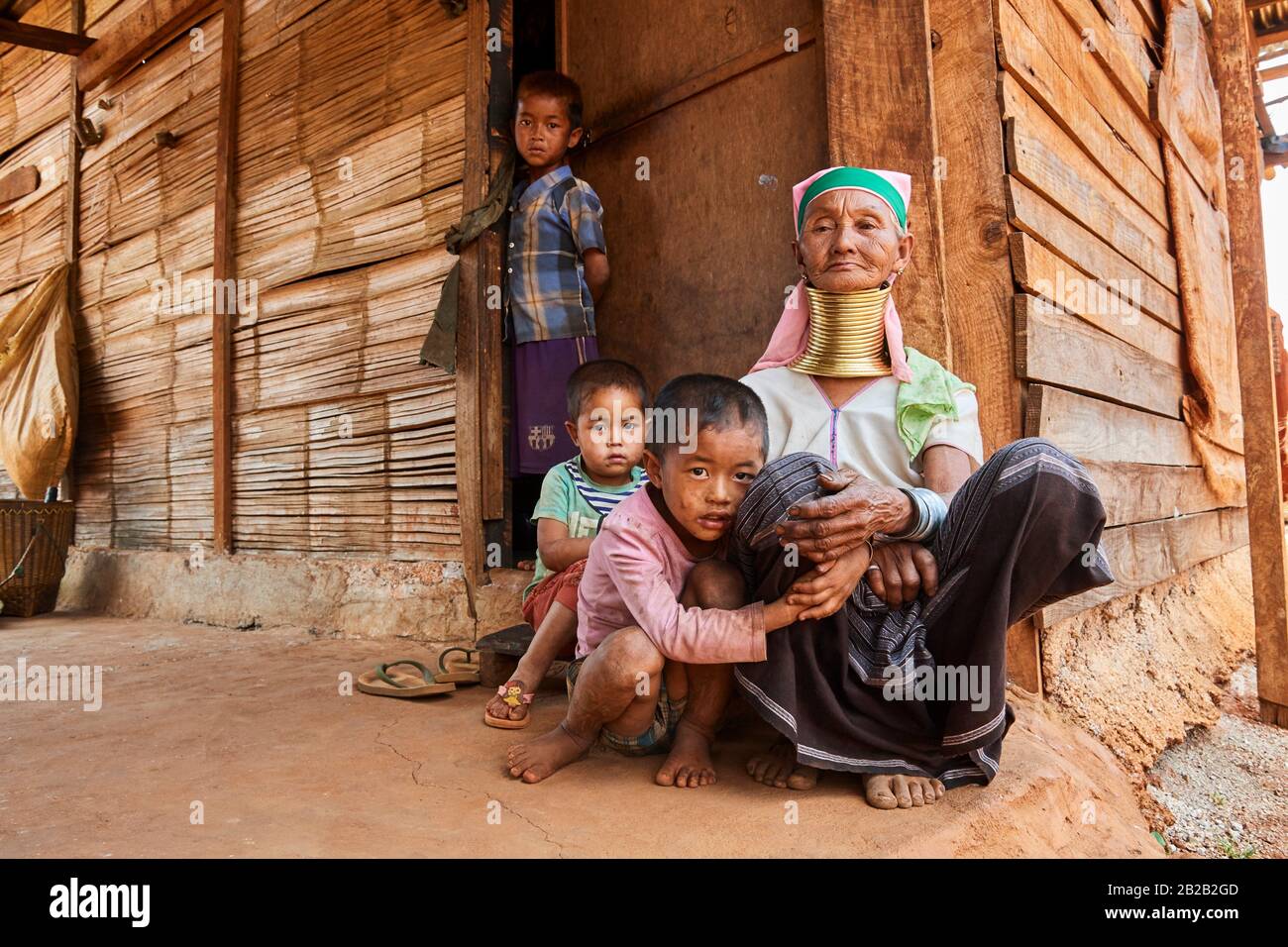 Kayan Lahwi mujer con bobinas de latón cuello y ropa tradicional cuidando de sus nietos mientras los padres están trabajando en la granja. El Largo Foto de stock