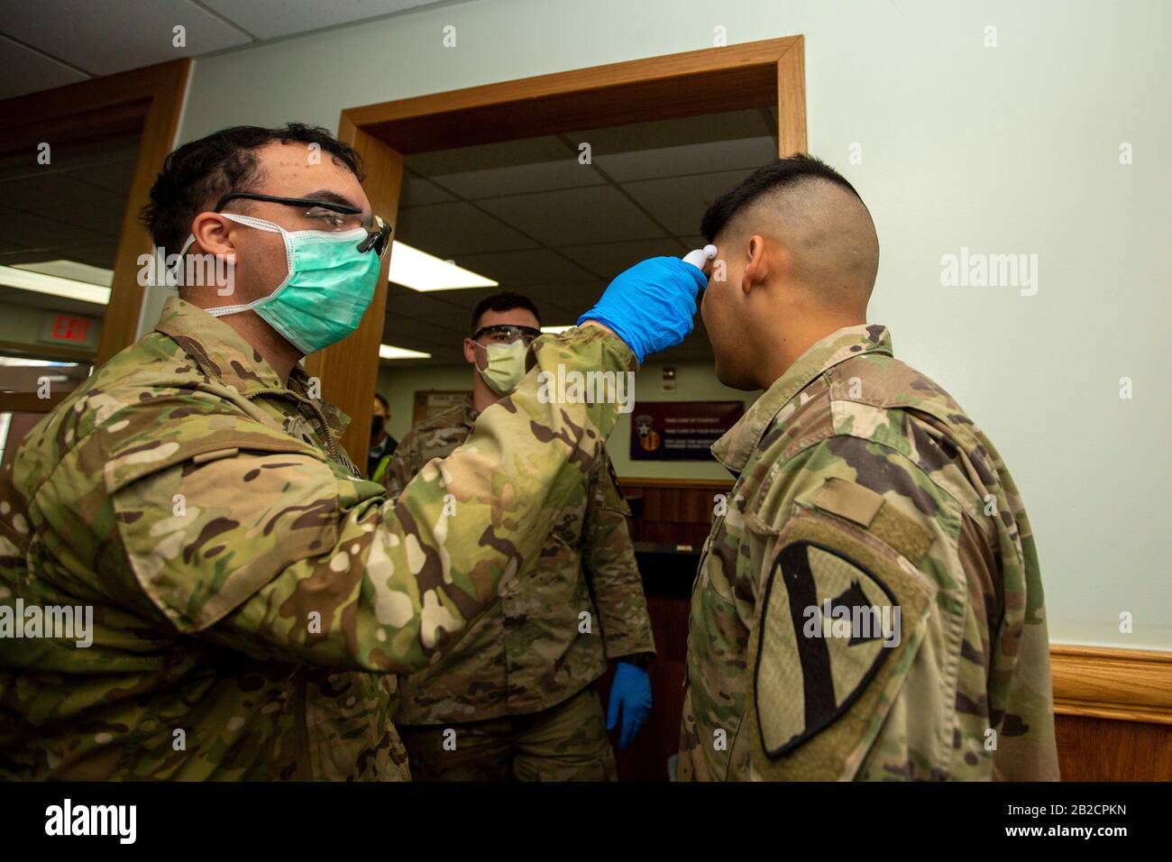 Un médico del ejército estadounidense examina a un compañero soldado para el COVID-19, usando un termómetro en la entrada de la guarnición del ejército Casey, el 26 de febrero de 2020 en Dongducheon, Corea del Sur. El brote de un nuevo coronavirus en Corea del Sur es el segundo de China. Foto de stock