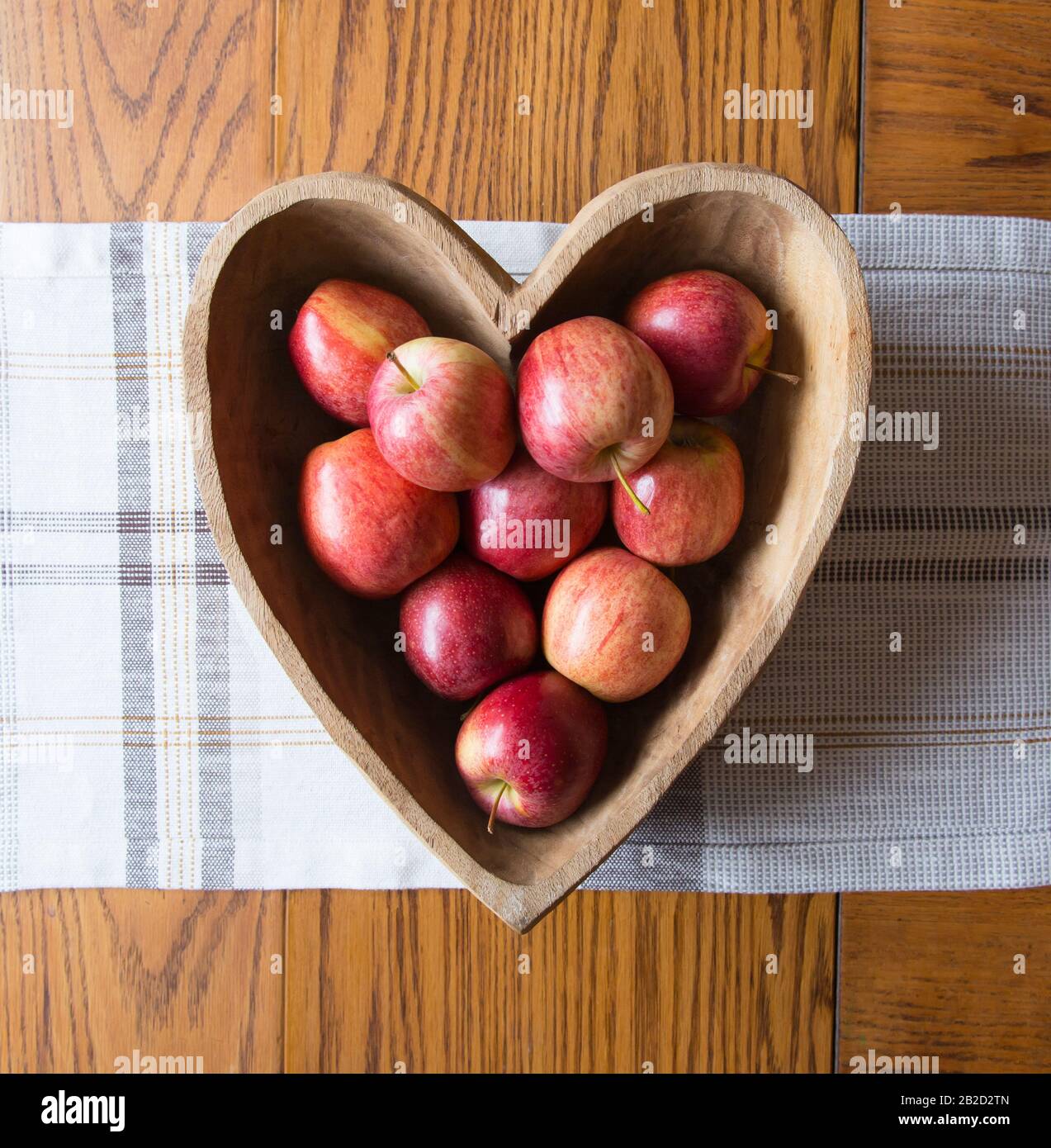 Cuenco de madera con forma de corazón y manzanas rojas Foto de stock