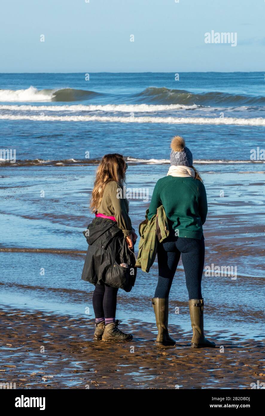 Dos mujeres jóvenes o niñas adolescentes con ropa de invierno caminando en  una playa en la costa viendo las olas rodar en la orilla Fotografía de  stock - Alamy