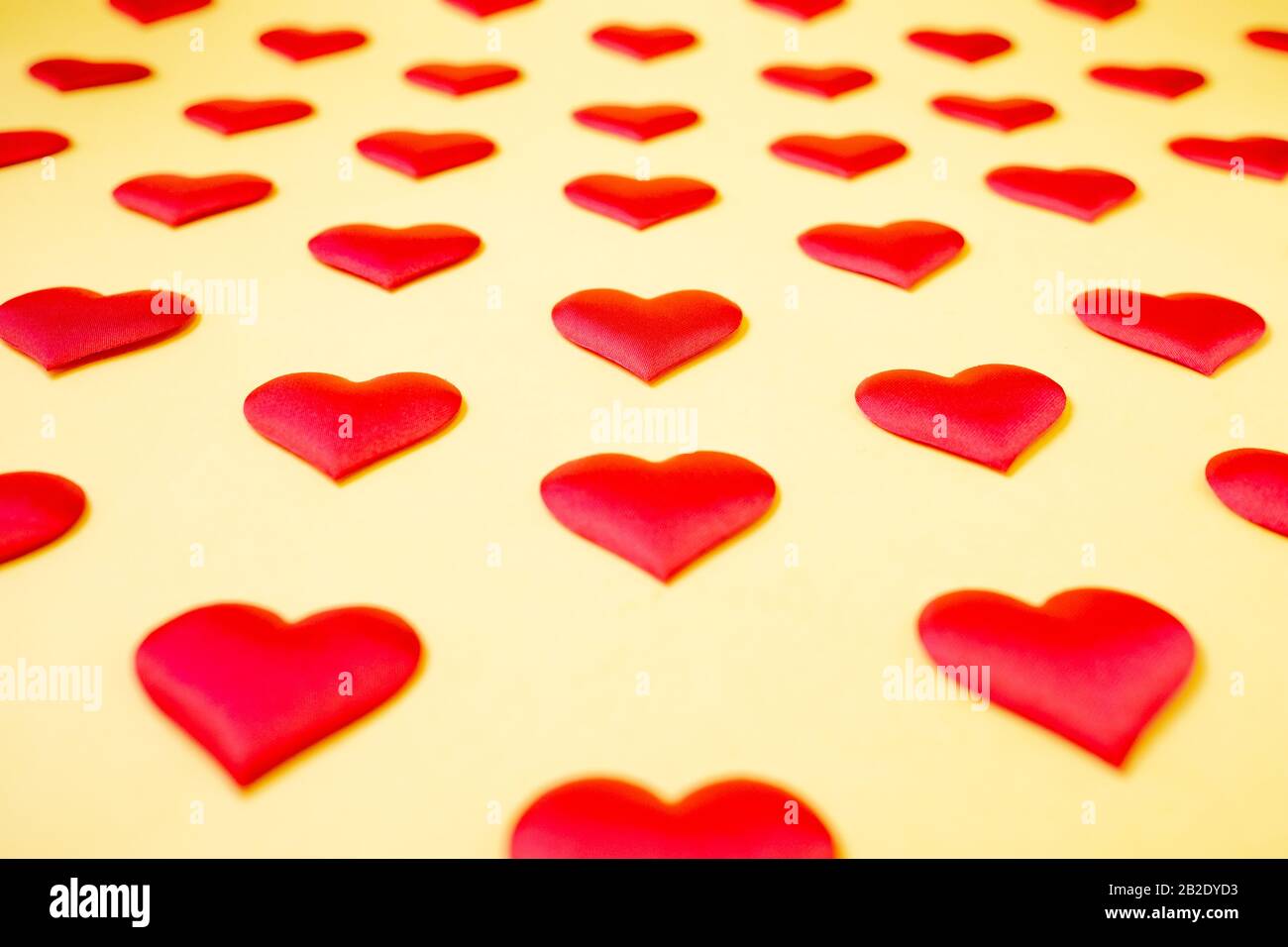 Muchos corazones de seda roja idénticos que se encuentran escalonados sobre un fondo amarillo. Símbolo de amor, ternura y pasión. Foto de stock