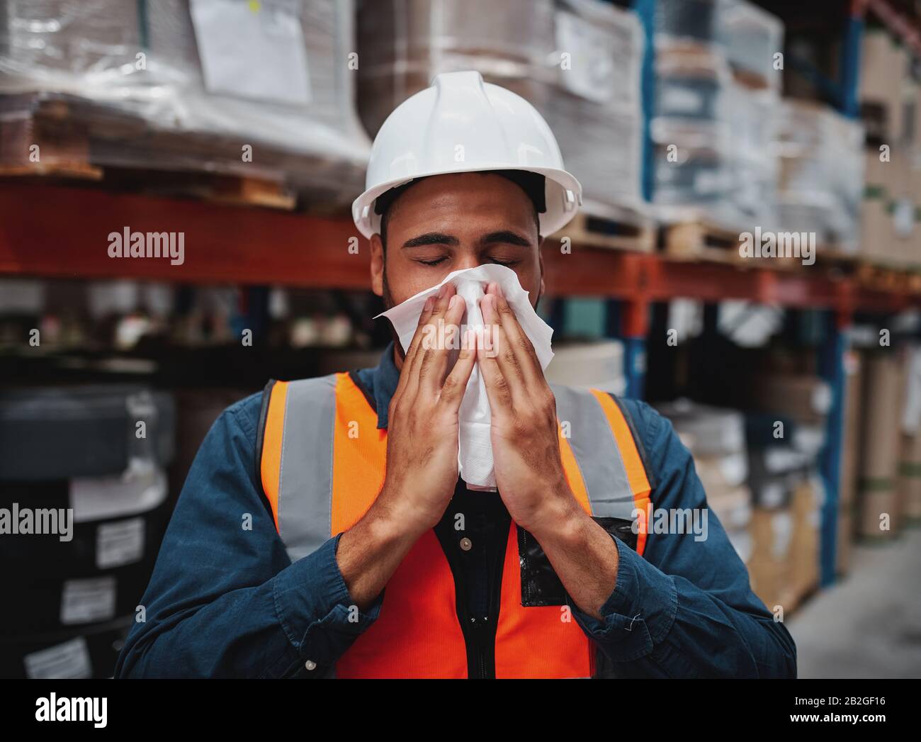 Joven gerente africano tosiendo y sintiéndose enfermo mientras cubría la boca con pañuelo en el almacén Foto de stock