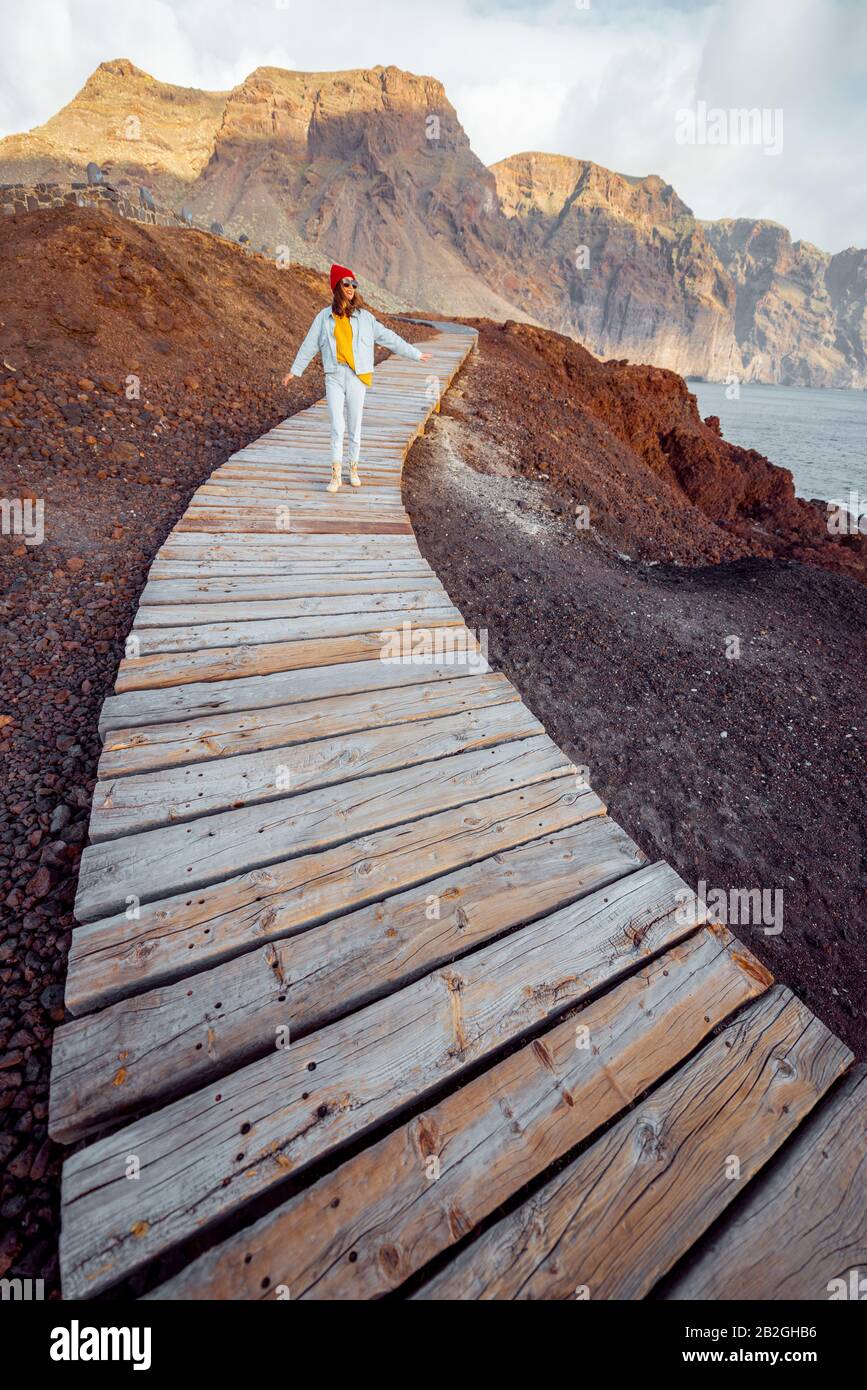 Mujer caminando por el pintoresco camino de madera a través de la tierra rocosa con montañas en el fondo. Viajando por el noroeste de la isla de cabo de Tenerife, España Foto de stock