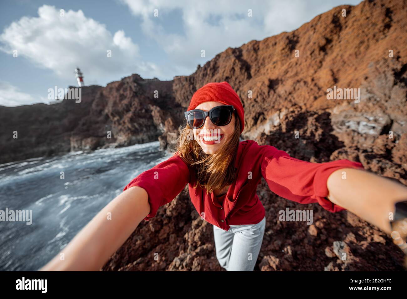 Joven mujer con estilo haciendo un retrato selfie mientras viaja por la costa rocosa del océano cerca del faro en la isla de Tenerife, España Foto de stock