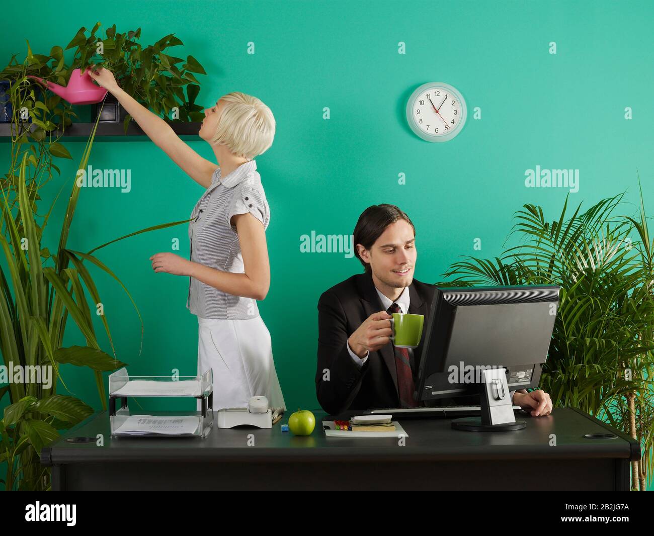 Hombre y mujer en la oficina hombre en el escritorio mujer riego plantas Foto de stock