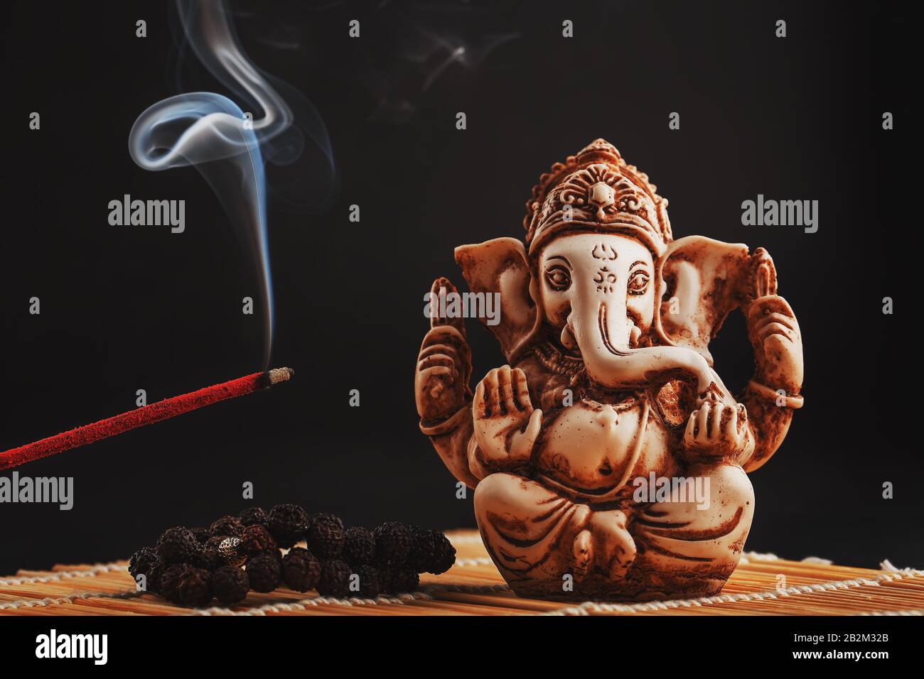 dios hindú Ganesh sobre un fondo negro. Estatua de Rudraksha y rosario en una mesa de madera con un palo de incienso rojo y humo de incienso. Espacio de copia Foto de stock