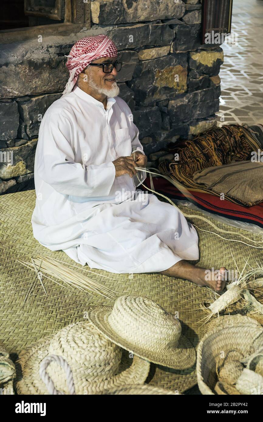 Dubai, EAU - 4 DE DICIEMBRE de 2017: El hombre mayor está tejiendo sombreros  de paja para reunirse con los invitados en el pabellón de los Emiratos  Árabes Unidos, Global Village Fotografía