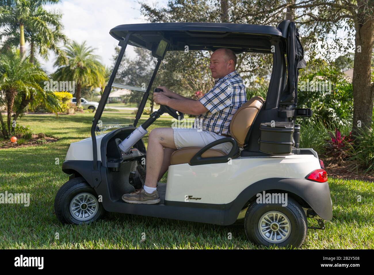 Un hombre que lleva una camisa de cuadros conduce un carrito de golf Club Car Tempo a través de la hierba de una casa de Palm City, Florida. Foto de stock