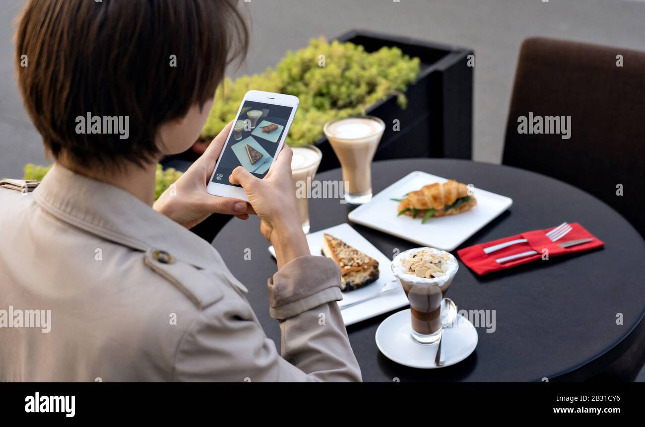 Milenial blogger niña tomando foto de comida en el teléfono en el café, closeup. Foto de stock