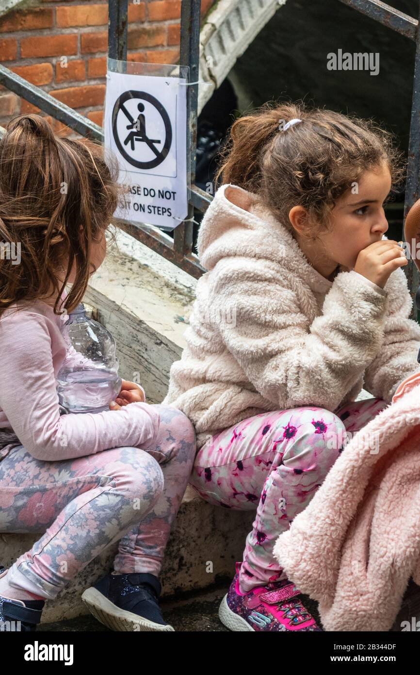 Los niños sentados en los pasos del canal comiendo llevar la comida. Nuevas leyes en Venecia Italia contra los turistas que se comportan mal. Incluyendo no sentarse en los escalones de los puentes de piedra. Se emitirán multas. Foto de stock