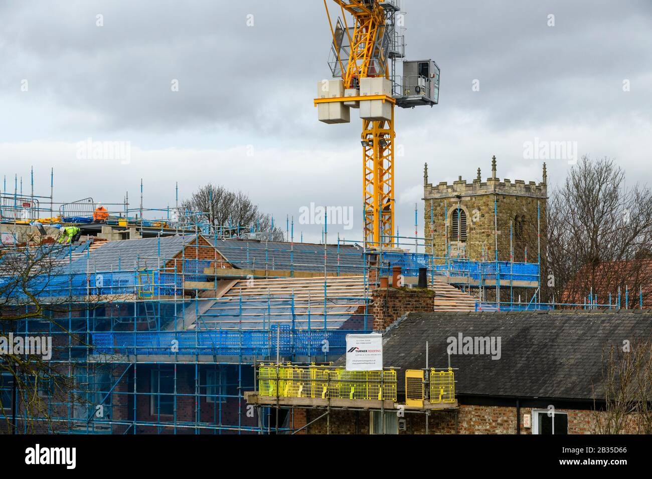 Sitio de construcción (techadores trabajando, techo de baldosas, grúa amarilla, cabina y mástil del operador, andamiaje) y torre de la iglesia - York, North Yorkshire, Inglaterra, Reino Unido. Foto de stock