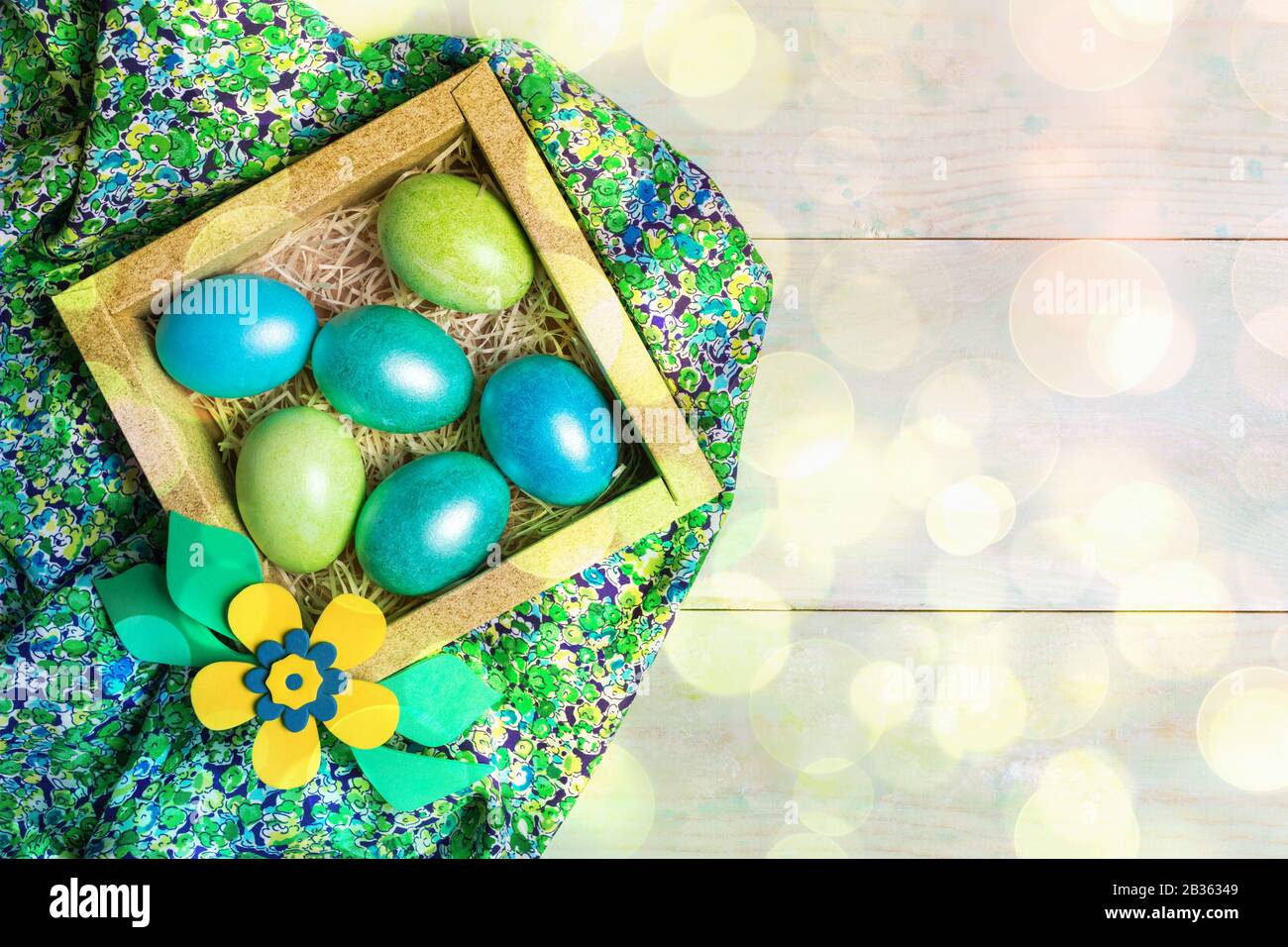 Decoración de Pascua de bricolaje. Huevos coloreados en caja cuadrada de  cartón con flor sobre tela floral verde sobre fondo de madera con bokeh.  Pascua de fondo. Hasta Fotografía de stock -