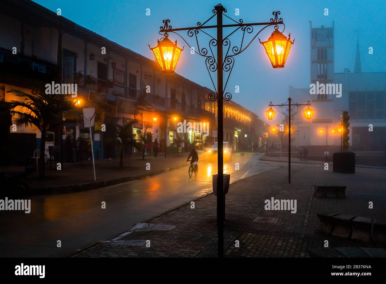Las lámparas decorativas de la calle se ven brillando en la plaza principal durante la brumosa caída nocturna en Sonsón, Colombia. Foto de stock