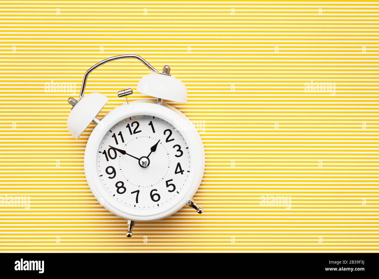 Reloj despertador blanco vintage sobre fondo amarillo. Vista superior, espacio de copia. Concepto de horario de verano. Foto de stock