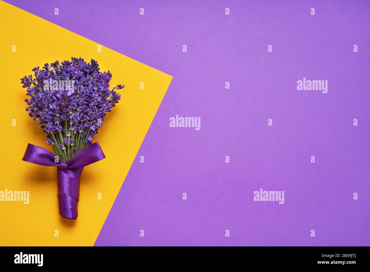 Ramo de hermosas flores de lavanda decoradas con cinta sobre fondo amarillo-púrpura. Vista superior, espacio de copia para texto. Foto de stock