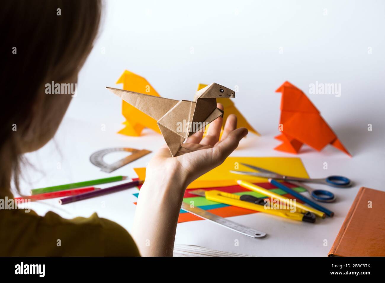 niña hace origami dinosaurio de papel coloreado. papel, regla, lápices,  cuchillo. interesante afición Fotografía de stock - Alamy