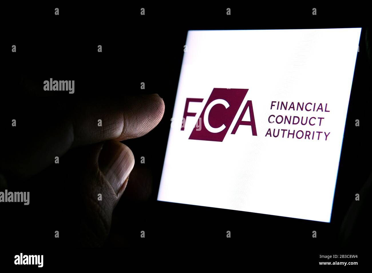 Logotipo de FCA Financial Conduct Authority en el smartphone y dedo apuntando a él en la habitación oscura. Concepto. FCA es un organismo regulador financiero en el Reino Unido Foto de stock