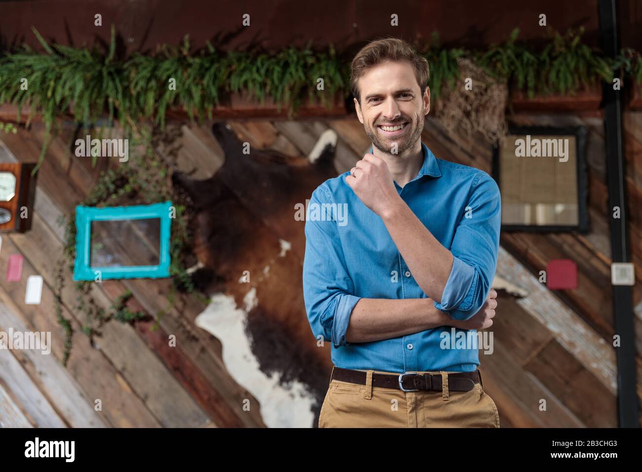 Hombre casual positivo riendo mientras que usa una camisa azul y marrones, parado en un fondo de café Fotografía de - Alamy