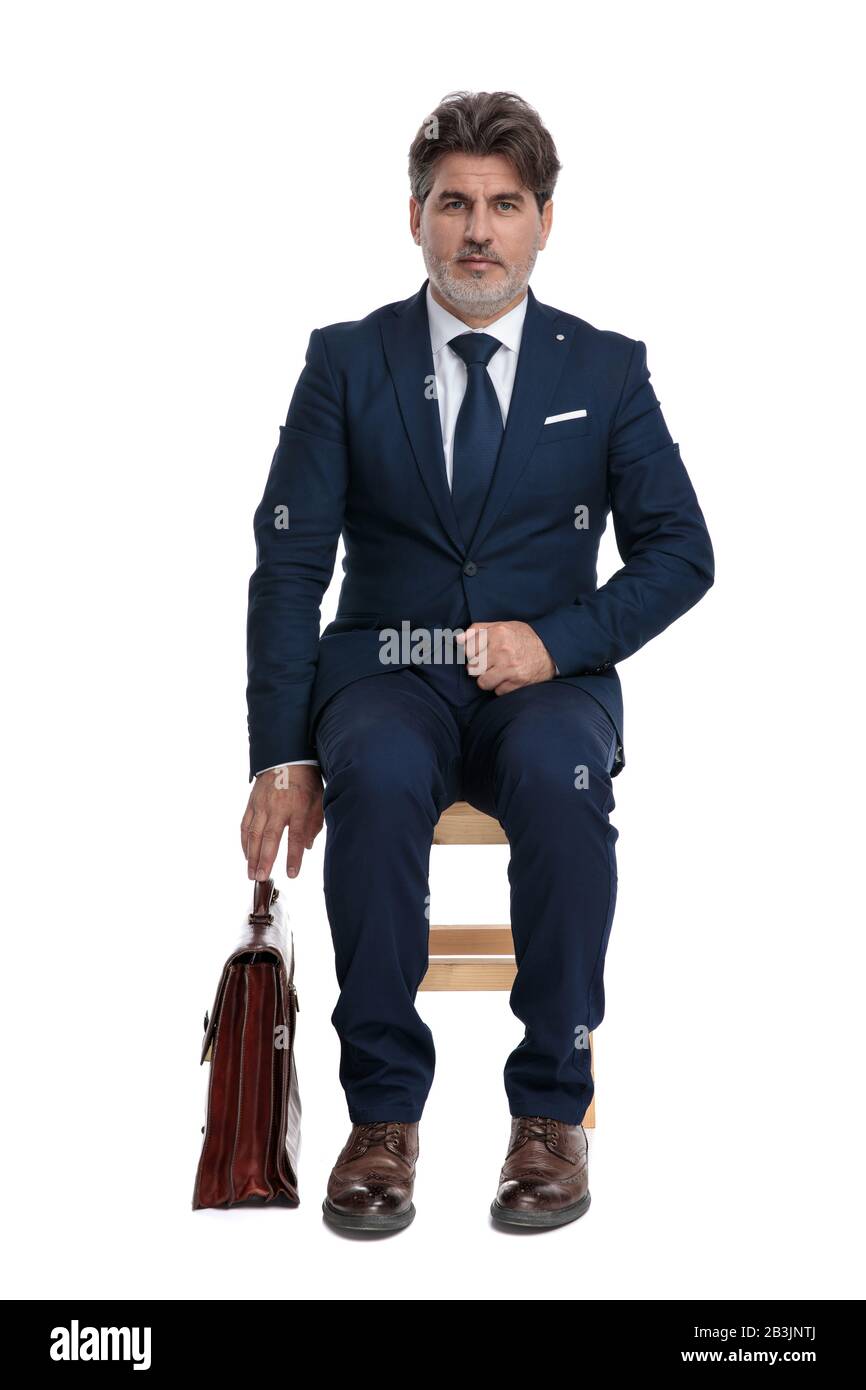 elegante hombre de negocios formal con traje azul marino sentado listo para  agarrar su maletín serio sobre fondo blanco de estudio Fotografía de stock  - Alamy