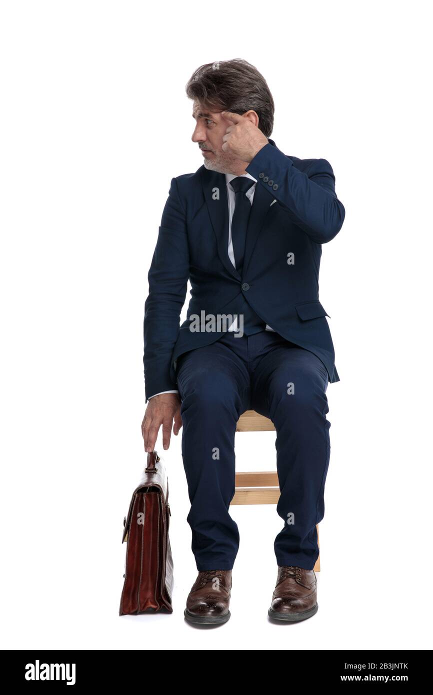intrigado hombre de negocios formal con traje azul marino y maletín está  sentado y haciendo un gesto loco a un lado en el fondo blanco del estudio  Fotografía de stock - Alamy