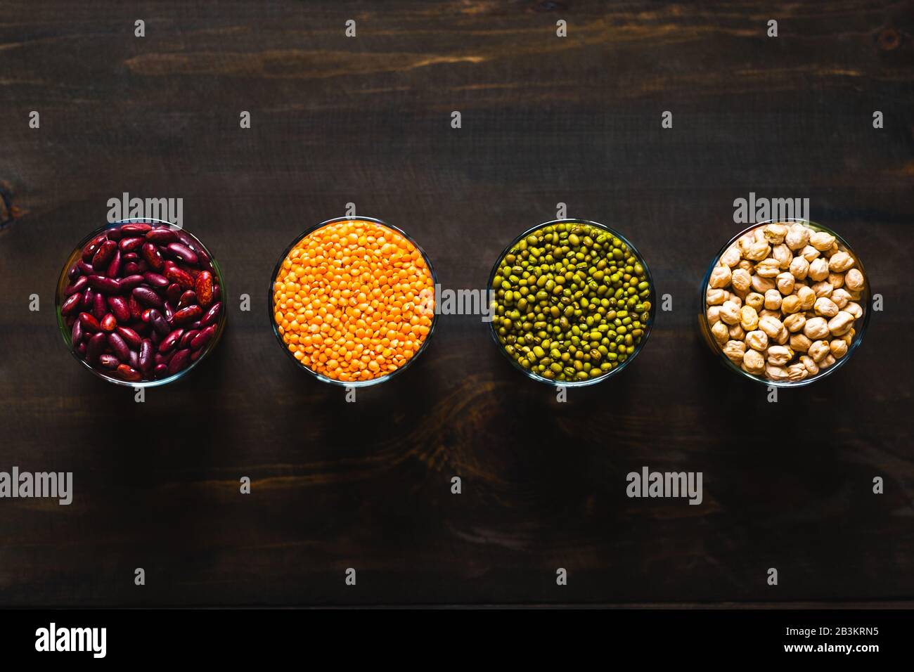 Conjunto de diferentes cereales y legumbres en un cuenco de cristal sobre una mesa negra, vista superior. Concepto de alimentos saludables para la nutrición. Frijoles, garbanzos, lentejas y mung b Foto de stock